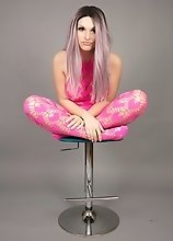 Bailey Jay in pretty pink behind gray background shows off as she strokes her hard massive dick